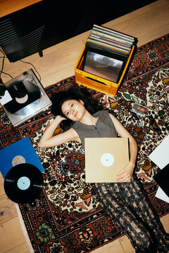 High angle view of young woman lying down with record vinyls on carpet at home