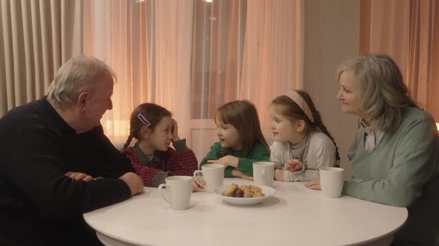 Happy Grandparents and Grandchildren Enjoying Tea and Cookies, Sharing Laughter and Conversation at Home
