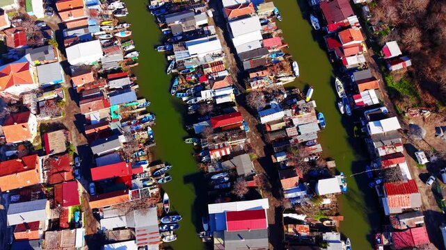 Drone shot of colorful rooftops and small boats parked in narrow green water canals. Top down view of fishing boats in water canals.