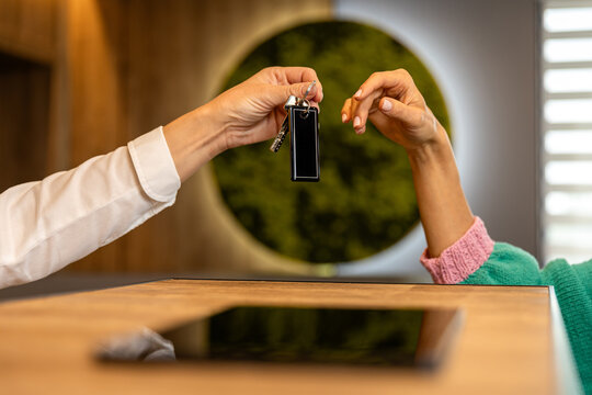 Hotel receptionist handing room key to guest at reception desk close up