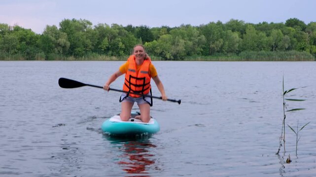 Woman paddling a stand up paddleboard on a lake outdoors. water sport, active leisure, summer vacation, nature fitness, scenic water.
