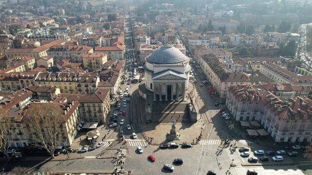 Aerial drone shot shows the neoclassical Gran Madre di Dio church and surrounding city blocks with traffic in Turin, Italy, historical landmark architecture, urban panoramic scene.