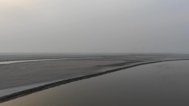 aerial drone footage of a River channels meandering through a hazy, flat landscape at sunrise, showing the effects of erosion and sediment deposition High quality drone 4k footage