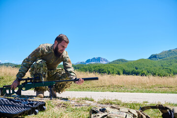 Obraz premium Military Sniper Soldier Preparing Rifle in Open Field Landscape
