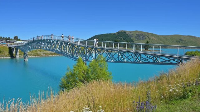 Eine Br&uuml;cke &uuml;ber einen See mit Menschen, umgeben von Bergen und dem klaren Himmel, Lake Tekapo, Tekapo, Canterbury, S&uuml;dinsel, Neuseeland, Ozeanien