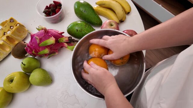 The hands of a woman in an apron standing in front of a table with fruit and washing mandarins