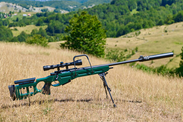 Bolt-Action Sniper Rifle With Scope and Suppressor On Bipod In Open Grassland Hunting Field