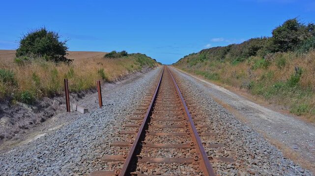 Eisenbahnschienen winden sich durch offene Felder unter einem hellblauen Himmel, Scarborough, Timaru, S&uuml;dinsel, Neuseeland, Ozeanien