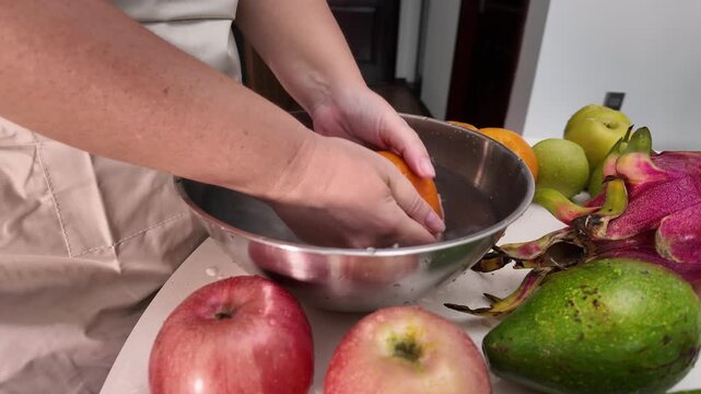 The hands of a woman standing in front of a table with fruit and washing mandarins in a bowl