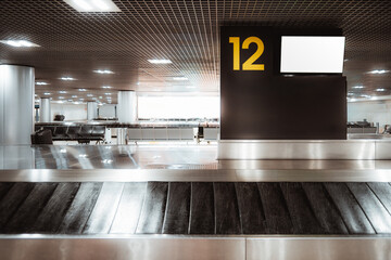 Airport baggage claim area with luggage carousel and large blank digital screen mockup on sign number 12, modern terminal interior, metal reflections, LCD mock-up screen on the top right © skyNext