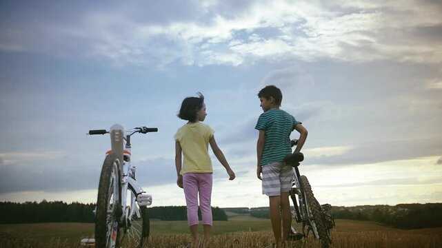 Golden Hour Bond: Children Sharing a Warm Hug After a Sunset Bike Ride in the Field