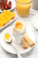 Tasty breakfast with soft boiled egg and toasted bread served on white marble table, closeup