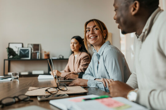 Smiling businesswoman looking at male colleague while sitting at table during team meeting in office