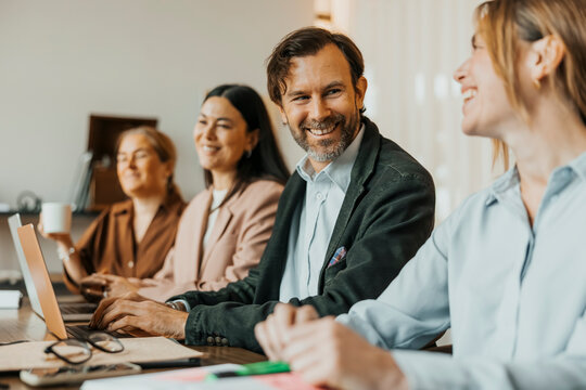 Smiling male entrepreneur talking with female coworker during group meeting in office