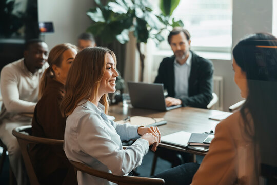 Smiling businesswoman interacting with coworkers sitting in meeting room