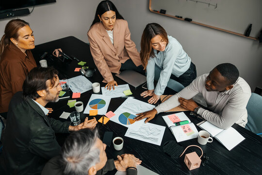 High angle view of business professionals discussing over documents while sitting around table in meeting room at office