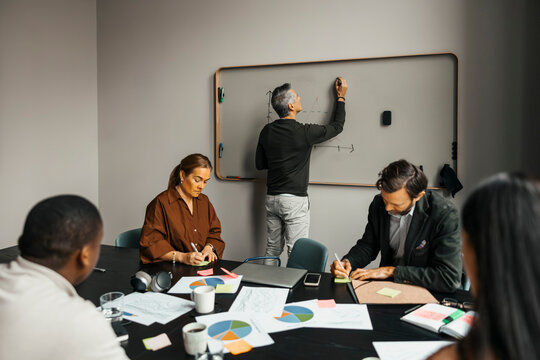 Rear view of senior businessman writing on whiteboard in team meeting at office