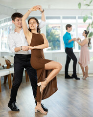 Fototapeta premium While doing rehearsal of reporting concert, guy and girl participants of dance workshop perform quickstep. Two couples practice their skills in performing quickstep during attending dancing school.