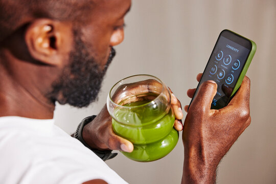 High angle view of active man drinking healthy juice while examining body health data on smart phone