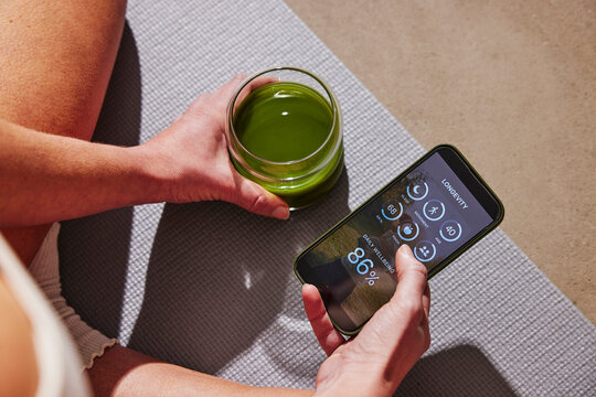High angle view of woman examining body scan health data on smart phone while sitting with detox juice
