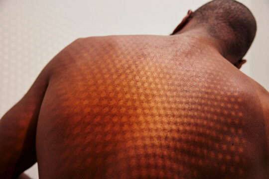Rear view of patterned shadow of sunlight on shirtless man