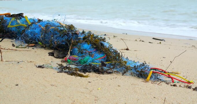 Wide beach scene with tangled net blue synthetic fibers, colorful ropes, scattered seaweed, gentle surf in background, urgent tone for cleanup campaigns and ecological rescue planning