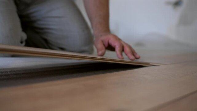 Worker aligning and clicking laminate floor panels together. The master uses a brush to remove dust from the joints of the laminate plate