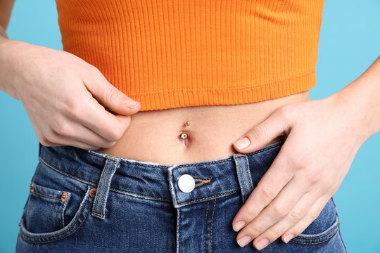 Woman with belly button piercing on light blue background, closeup