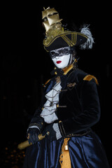 Obraz premium Venice, Italy - February 11, 2026: Elegant masked figure in elaborate costume with gold accents and feathered hat at Venice Carnival night celebration