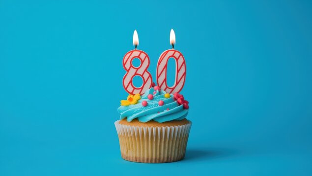 Cupcake with lit candles shaped like the number 80 on a blue backdrop, for a celebration