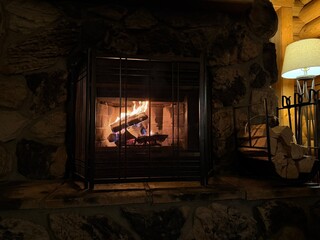 Naklejka premium Fireplace, firewood and lamp indoors. Cozy atmosphere