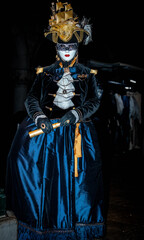 Obraz premium Venice, Italy - February 11, 2026: Elegant masked figure in elaborate blue gown and hat, holding a golden object at the Venice Carnival night celebration