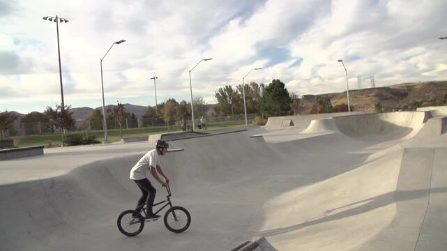 A slow motion footage of a young Caucasian man doing bicycle jumping in a skate park at sunset