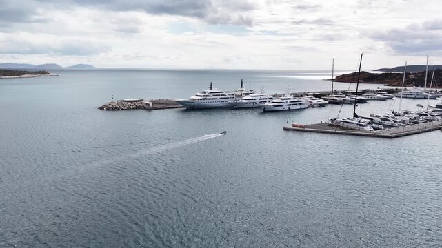 Aerial view of Vouliagmeni Nautical Club luxury yacht marina near Temple of Apollo Zoster with superyachts docked in calm Mediterranean waters, Greece
