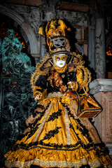 Obraz premium Venice, Italy - February 11, 2026: Elaborate Venetian carnival costume featuring intricate yellow and black design with feathers and mask, set against historic architecture