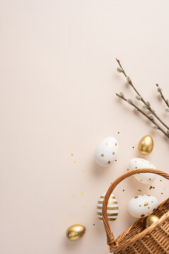 Happy Easter vertical greeting featuring a gold polka dot egg and striped egg spilling from a wicker basket beside a pussywillow branch on a soft beige background for spring celebration