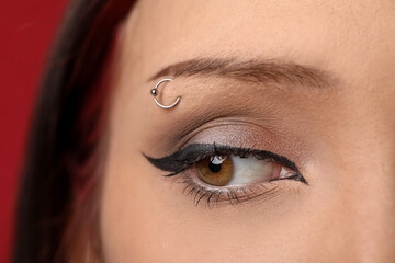 Fototapeta premium Woman with eyebrow piercing and perfect makeup on red background, closeup