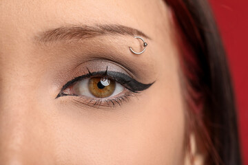 Obraz premium Woman with eyebrow piercing and perfect makeup on red background, closeup
