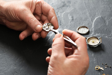 Senior man fixing mechanism of vintage wrist watch at black table, closeup