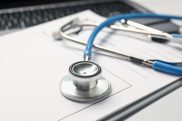 Stethoscope, laptop and clipboard on light grey table, closeup