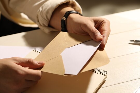 Man opening envelope with letter at wooden table indoors, closeup