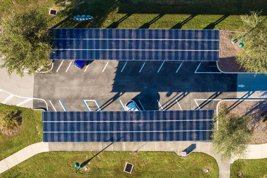 Solar power generation technology integrated in urban infrastructure. Photovoltaic panels installed as shade roof over parking lot with parked cars for effective production of clean energy.