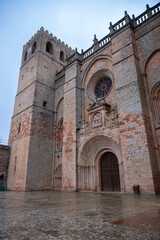 Obraz premium Majestic exterior of the Romanesque and Gothic cathedral in Siguenza Spain featuring a massive stone tower a decorative rose window and an ornate arched entrance on a rainy day in Guadalajara