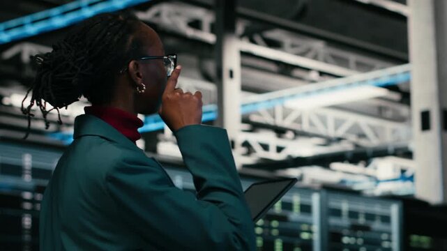 Data center programmer writing code for resource optimization using tablet application. African american woman walking in server hub using programming script on device to upgrade equipment, camera B