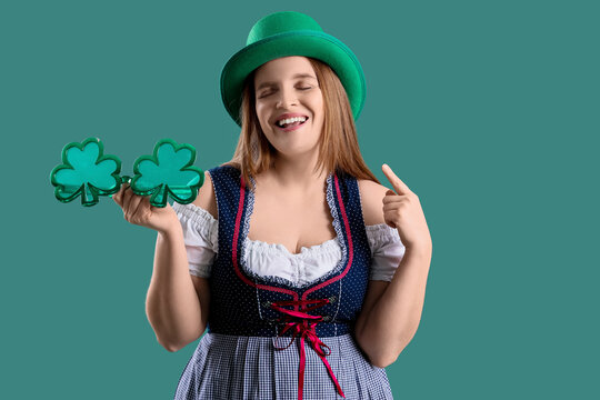 Redhead Irish waitress with clover shaped eyeglasses pointing at leprechaun hat on green background. St. Patrick's Day celebration