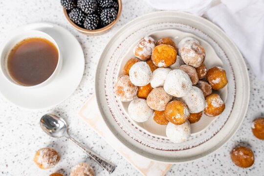 Plate of powdered sugar donut holes with coffee and blackberries