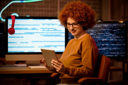 Young female programmer with tablet computer at her workspace in office at night