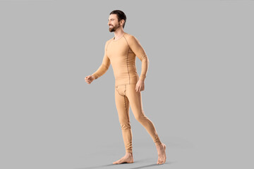 Fototapeta premium Handsome young man in thermal underwear walking on grey background