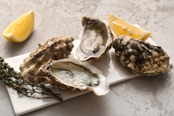 Board with delicious fresh oysters, thyme and lemon on grey background, closeup © Pixel-Shot