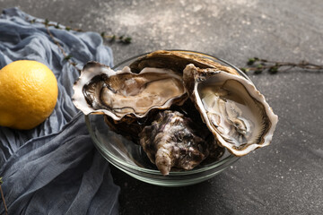 Glass bowl with delicious fresh oysters, lemon and thyme on dark background, closeup © Pixel-Shot